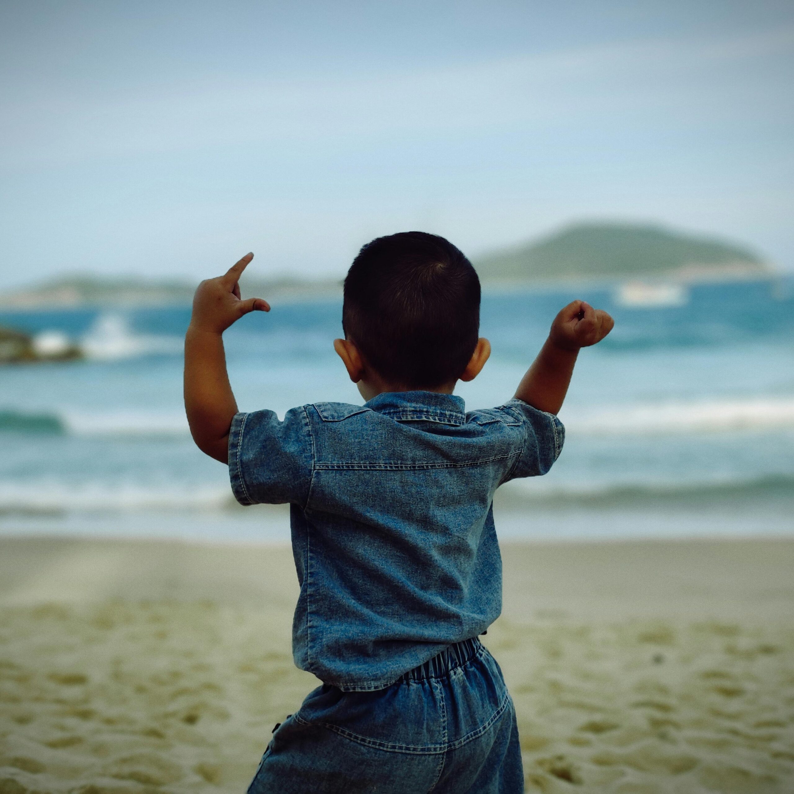 Back view of a child in denim at the beach in Phú Yên, Vietnam, celebrating the moment.