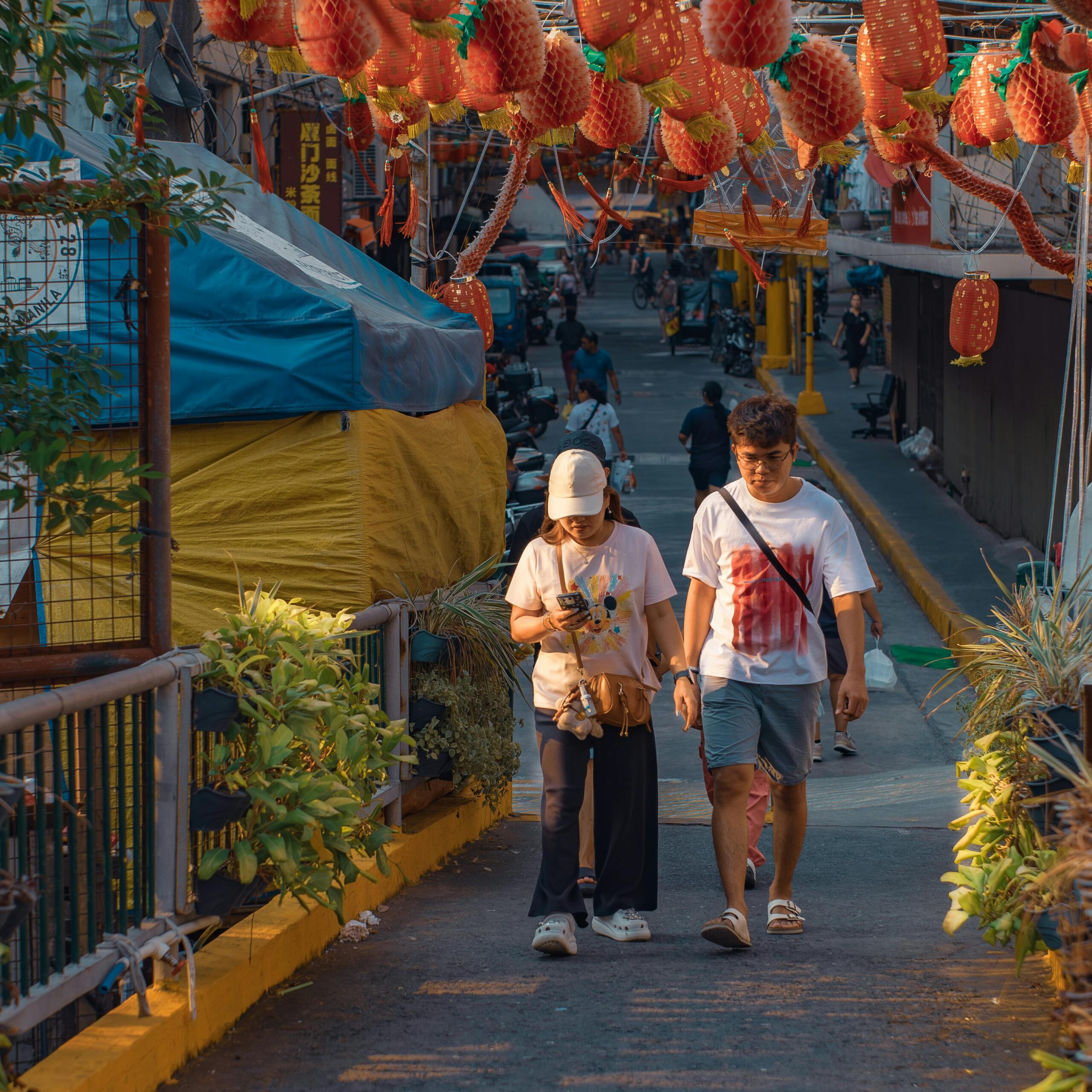 A couple strolls under vibrant red lanterns in an urban setting, evoking festive charm.