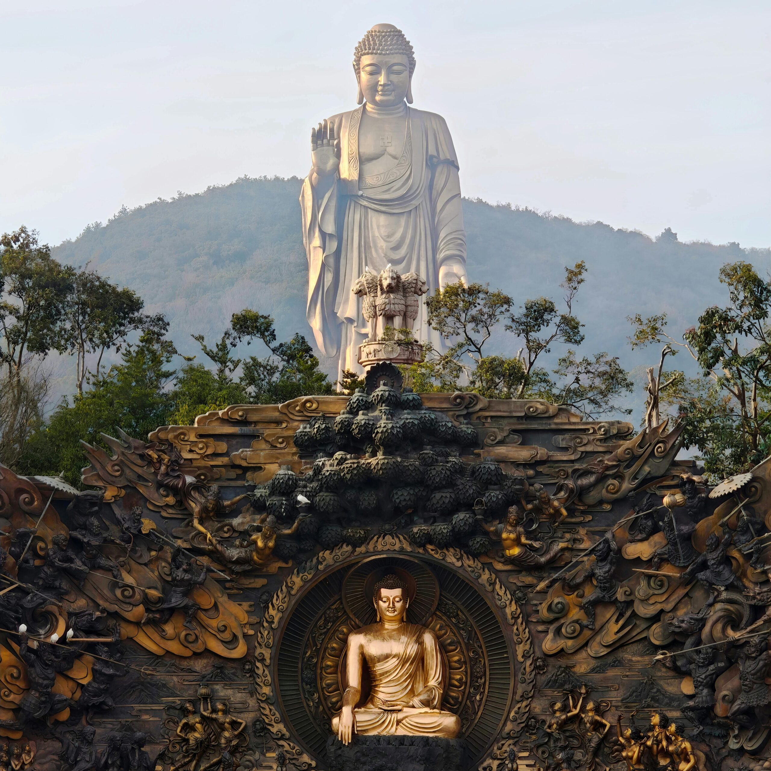 A towering Buddha statue stands amidst lush greenery and ornate carvings, exuding tranquility.