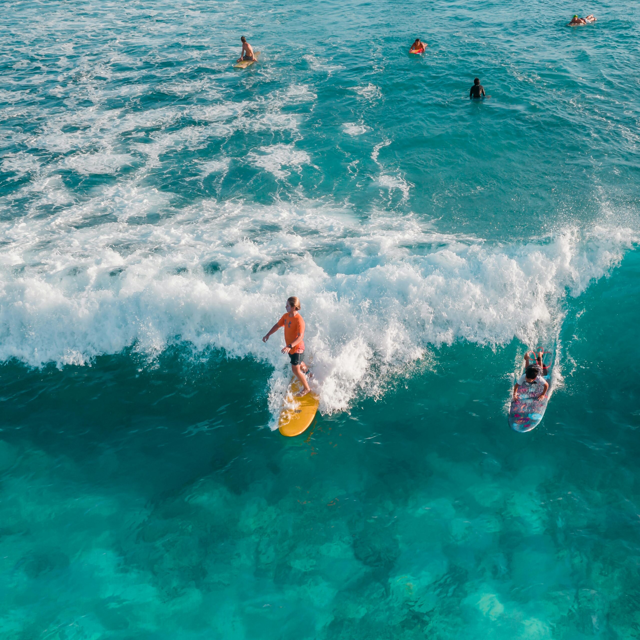 Surfers catch waves in vibrant blue Hawaiian ocean waters from above.