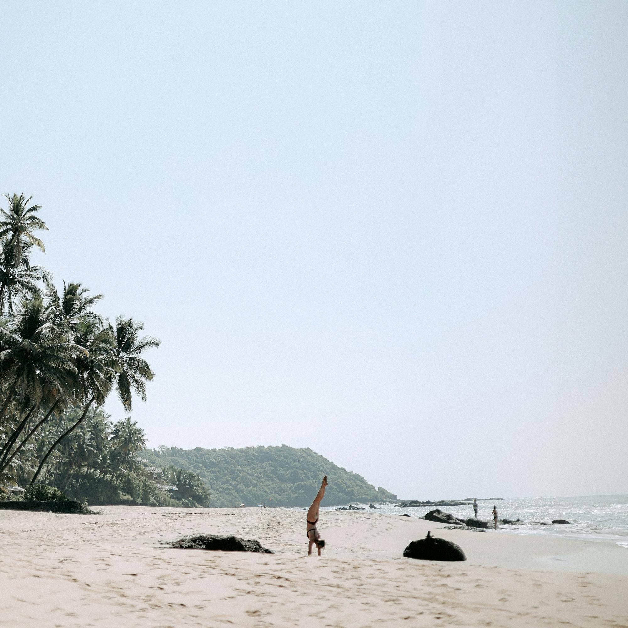A woman practicing yoga in a tropical beach setting with palm trees and blue sky.
