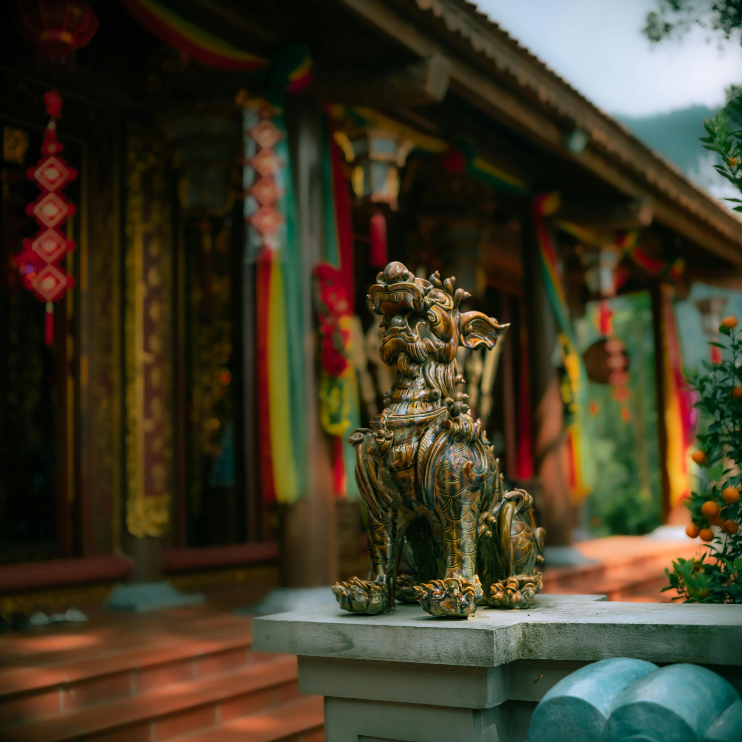A detailed bronze guardian lion statue in front of a colorful Asian temple with vibrant decor.