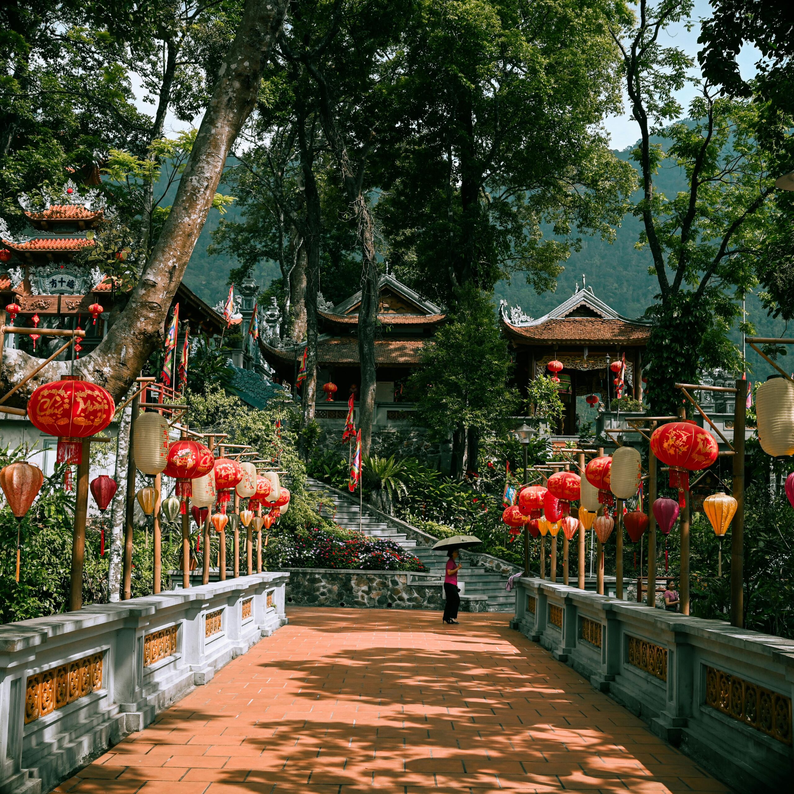 A serene temple path adorned with vibrant red lanterns in a lush forest setting.