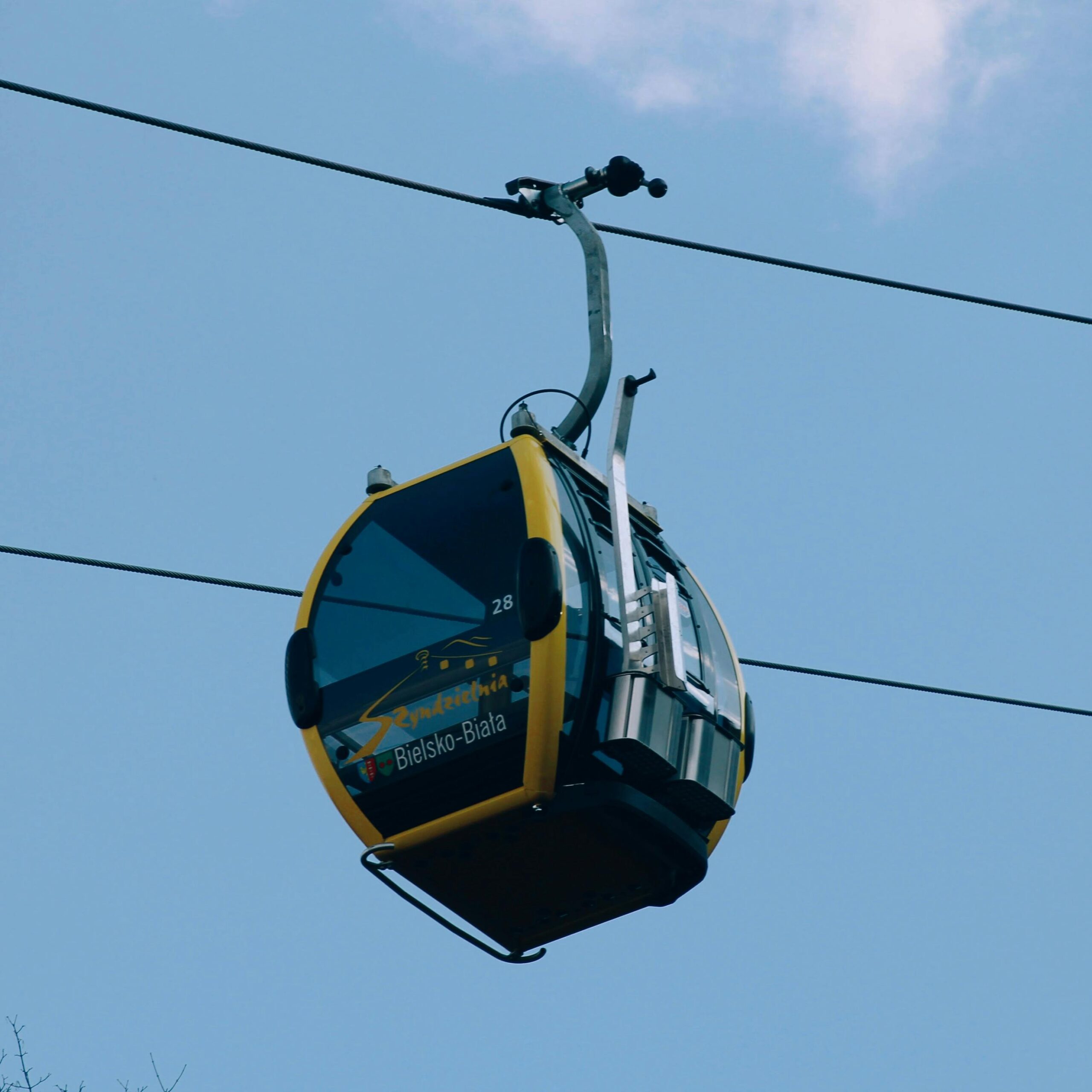 A gondola lift suspended in the sky in Bielsko-Biala, Poland against a bright blue background.