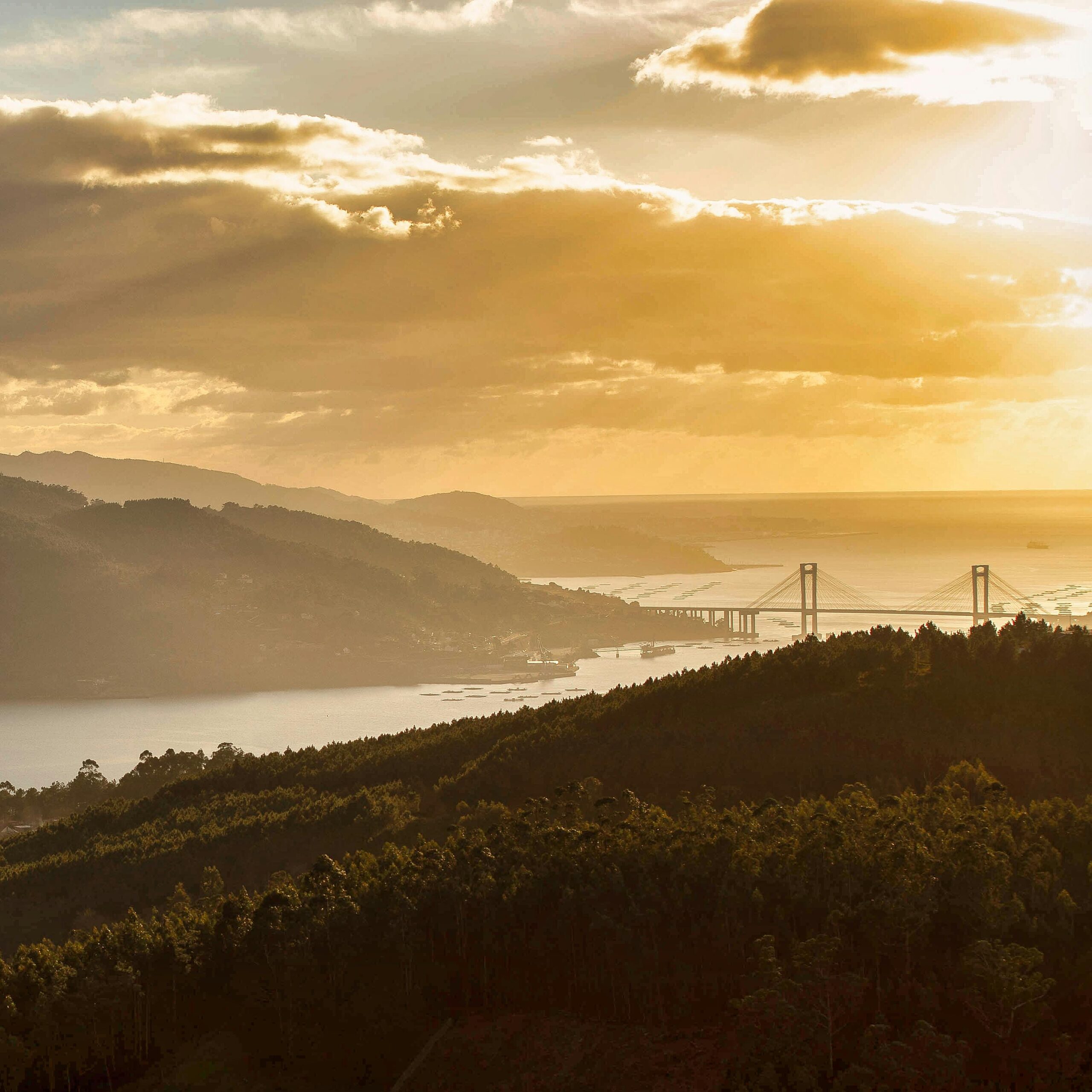 A stunning sunset over a scenic valley with a prominent bridge, capturing warm hues and dramatic skies.