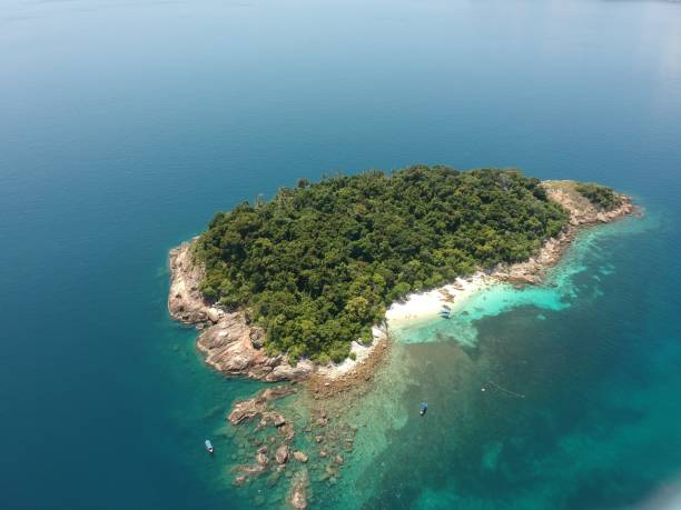 An aerial shot of the Perhentian Islands with green trees surrounded by the calm sea on a sunny day